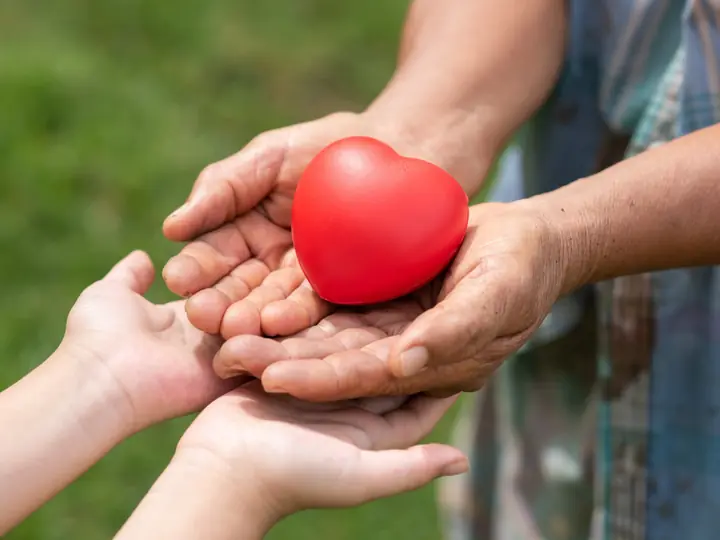 Older hands passing a red heart to a child’s hands